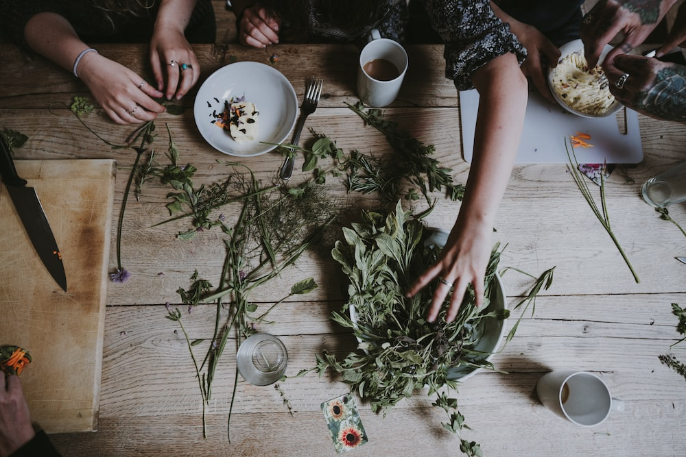 People’s hands on a wooden table with assorted herbs and eatables